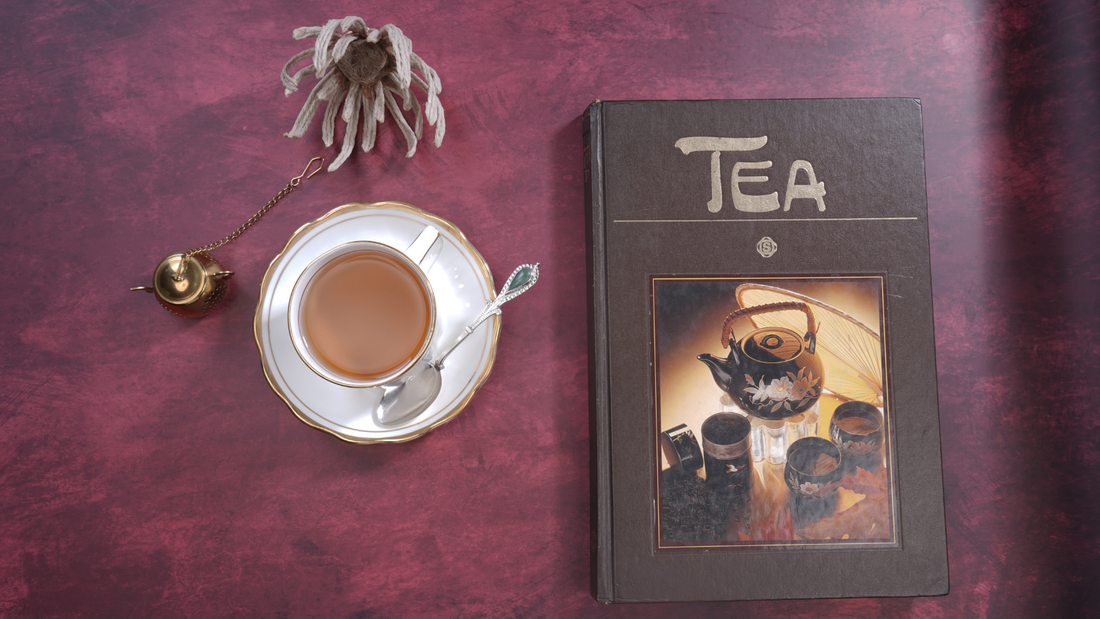 Flat lay of a tea cup, book and infuser on a maroon table