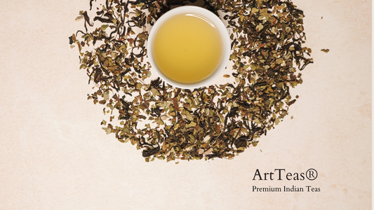 Golden brewed tea in a white cup surrounded by circular arrangement of loose leaf tea.