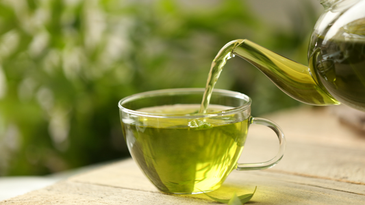 Freshly brewed green tea being poured into a glass cup from a teapot