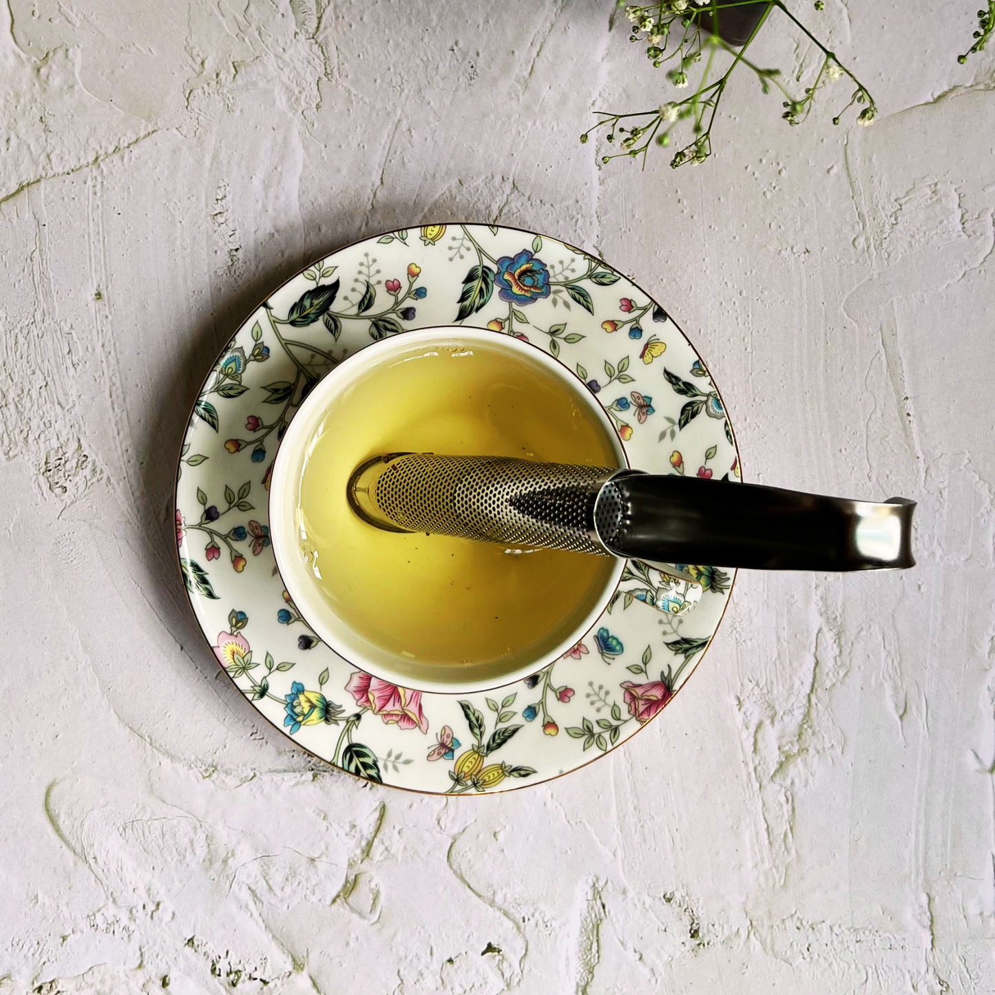 Tea cup with floral saucer and spoon on a textured white surface