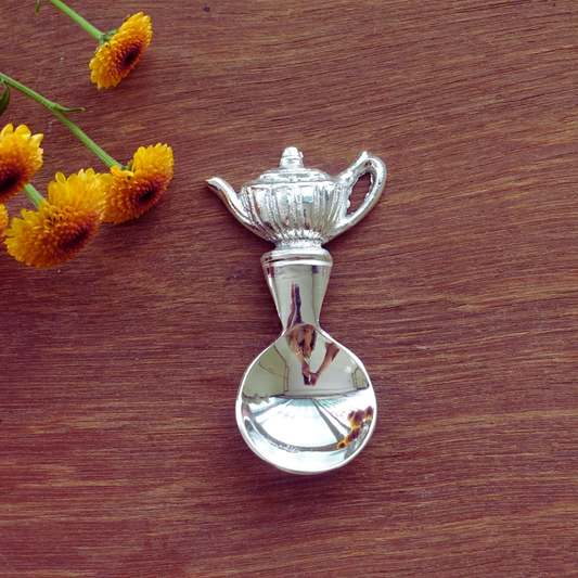 Tea measuring spoon with decorative silver teapot handle on dark background